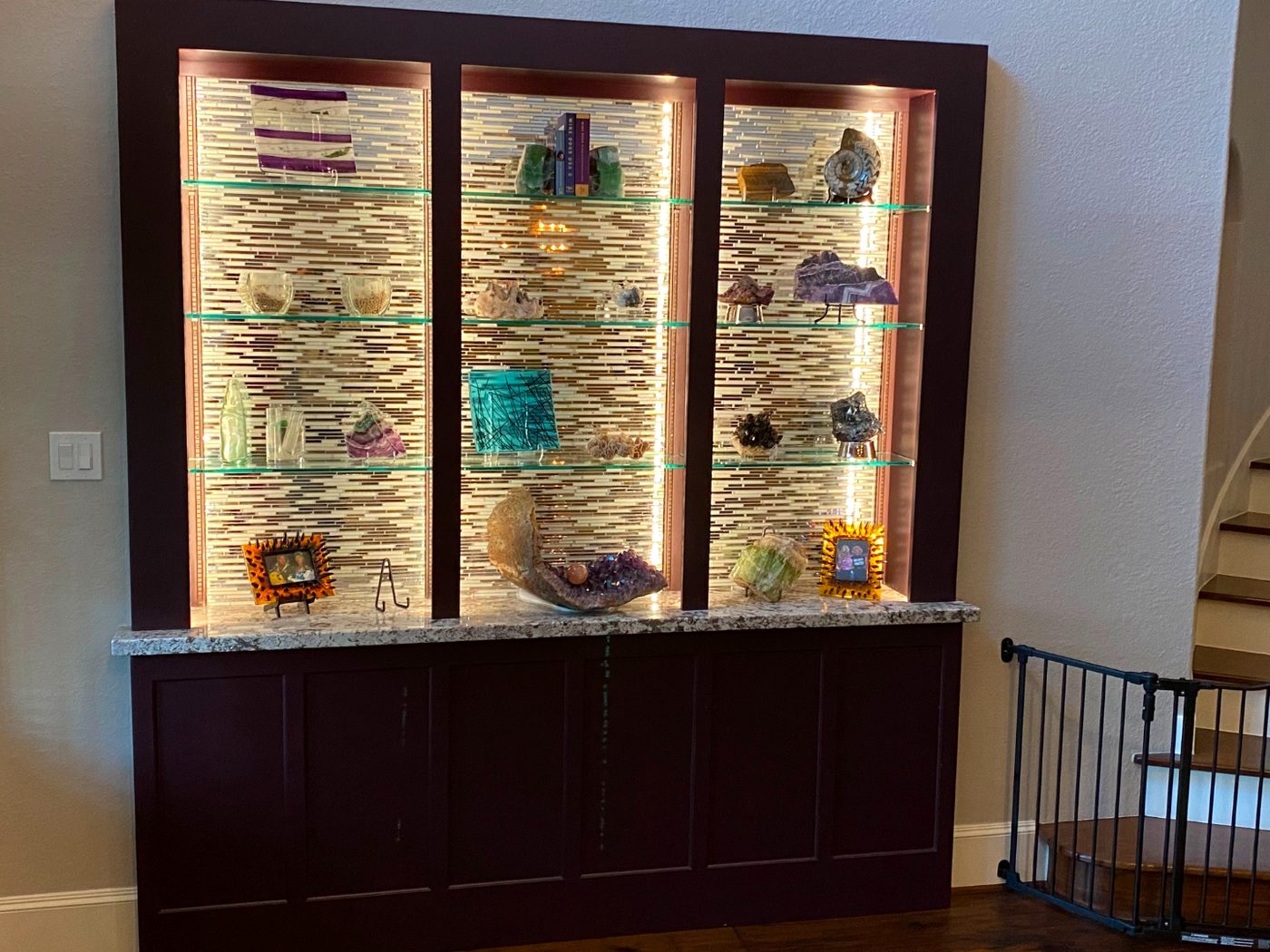 Custom lit display cabinet with glass shelves, mosaic tile back panel and granite top